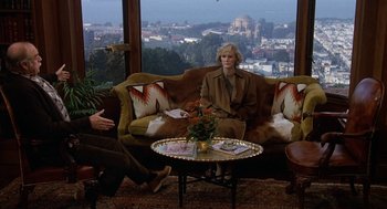 Movie still from “Jagged Edge” (1985), directed by Richard Marquand – Two people sitting on a couch in a living room; Wide shot, High angle
