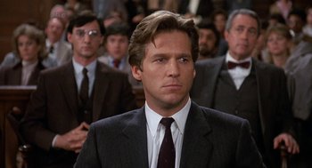 Movie still from “Jagged Edge” (1985), directed by Richard Marquand – A man in a suit and tie in front of a group of people; Close Up shot, Low angle