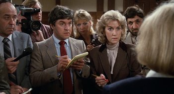 Movie still from “Jagged Edge” (1985), directed by Richard Marquand – A group of people standing in front of a camera; Medium shot, High angle