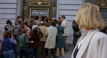 Movie still from “Jagged Edge” (1985), directed by Richard Marquand – A group of people standing outside of a city hall building; Wide shot, Over the shoulder angle