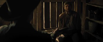 Movie still from “Jane Got a Gun” (2015), directed by Gavin O'Connor – A man sitting in front of a wooden wall; Medium shot, Over the shoulder angle