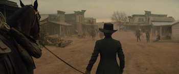 Movie still from “Jane Got a Gun” (2015), directed by Gavin O'Connor – A man in a black coat and a black hat holding a whip; Wide shot, Low angle