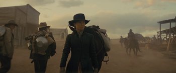 Movie still from “Jane Got a Gun” (2015), directed by Gavin O'Connor – A woman in a black hat and a black coat walking a horse in the desert; Medium shot, Low angle