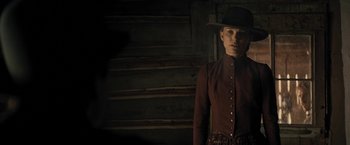 Movie still from “Jane Got a Gun” (2015), directed by Gavin O'Connor – A man in a cowboy hat standing in front of a wooden wall; Medium shot, Over the shoulder angle