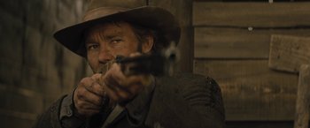 Movie still from “Jane Got a Gun” (2015), directed by Gavin O'Connor – A man holding a gun while wearing a cowboy hat; Close Up shot, Over the shoulder angle