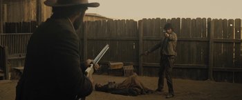 Movie still from “Jane Got a Gun” (2015), directed by Gavin O'Connor – Two men in cowboy garb holding guns in a fenced in area; Wide shot, Over the shoulder angle