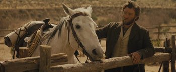 Movie still from “Jane Got a Gun” (2015), directed by Gavin O'Connor – A man standing next to a horse in a fenced in area; Medium shot, Over the shoulder angle