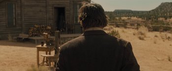 Movie still from “Jane Got a Gun” (2015), directed by Gavin O'Connor – A man standing in front of a wooden house; Medium shot, Over the shoulder angle