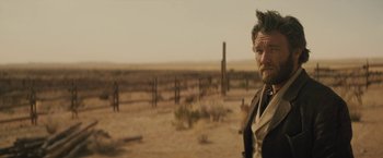 Movie still from “Jane Got a Gun” (2015), directed by Gavin O'Connor – A man standing in the middle of an empty field; Close Up shot, Over the shoulder angle