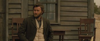 Movie still from “Jane Got a Gun” (2015), directed by Gavin O'Connor – A man with a long beard standing in front of a house; Medium shot, Over the shoulder angle