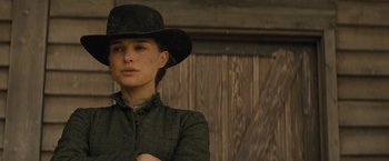 Movie still from “Jane Got a Gun” (2015), directed by Gavin O'Connor – A woman wearing a black hat standing in front of a wooden wall; Close Up shot, Over the shoulder angle