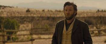 Movie still from “Jane Got a Gun” (2015), directed by Gavin O'Connor – A man with a beard standing in a field; Medium shot, Over the shoulder angle