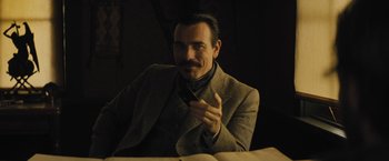 Movie still from “Jane Got a Gun” (2015), directed by Gavin O'Connor – A man in a suit and tie holding a cell phone; Medium shot, Low angle