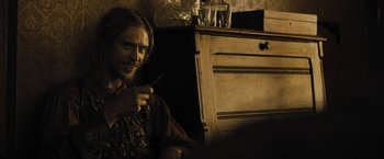 Movie still from “Jane Got a Gun” (2015), directed by Gavin O'Connor – A man sitting in front of a wooden dresser; Medium shot, Over the shoulder angle