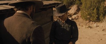 Movie still from “Jane Got a Gun” (2015), directed by Gavin O'Connor – A man and a woman sitting next to each other in front of a wooden structure; Medium shot, Over the shoulder angle
