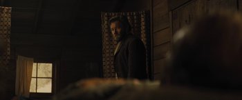 Movie still from “Jane Got a Gun” (2015), directed by Gavin O'Connor – A man standing in front of a wooden wall; Medium shot, Over the shoulder angle