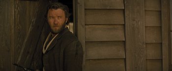 Movie still from “Jane Got a Gun” (2015), directed by Gavin O'Connor – A man standing in front of a wooden building; Close Up shot, Over the shoulder angle