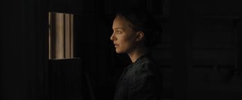 Movie still from “Jane Got a Gun” (2015), directed by Gavin O'Connor – A young woman is standing in a dark room; Close Up shot, Over the shoulder angle