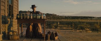 Movie still from “Jane Got a Gun” (2015), directed by Gavin O'Connor – A person sitting at a table with jars on top of it; Wide shot, Low angle