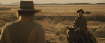Movie still from “Jane Got a Gun” (2015), directed by Gavin O'Connor – A man riding on the back of a brown horse; Wide shot, Over the shoulder angle