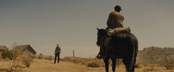 Movie still from “Jane Got a Gun” (2015), directed by Gavin O'Connor – A man riding a horse on a dirt field; Wide shot, Over the shoulder angle