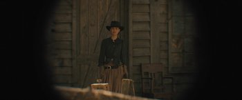 Movie still from “Jane Got a Gun” (2015), directed by Gavin O'Connor – A woman standing in front of a wooden building; Medium shot, Low angle