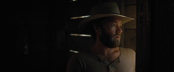 Movie still from “Jane Got a Gun” (2015), directed by Gavin O'Connor – A man with a beard and a hat in a dark room; Close Up shot, Over the shoulder angle