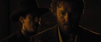 Movie still from “Jane Got a Gun” (2015), directed by Gavin O'Connor – A man with a beard and a hat in a dark room; Close Up shot, Over the shoulder angle