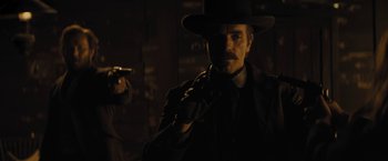 Movie still from “Jane Got a Gun” (2015), directed by Gavin O'Connor – A man in a hat is holding a gun; Medium shot, Low angle