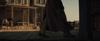 Movie still from “Jane Got a Gun” (2015), directed by Gavin O'Connor – A person walking down the sidewalk in front of a house; Wide shot, Low angle