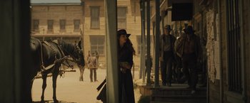 Movie still from “Jane Got a Gun” (2015), directed by Gavin O'Connor – A woman standing on the steps of an old western town; Wide shot, Over the shoulder angle