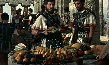 Movie still from “Jason and the Argonauts” (1963), directed by Don Chaffey – Two men in roman garb at an outdoor fruit stand; Medium shot, Over the shoulder angle