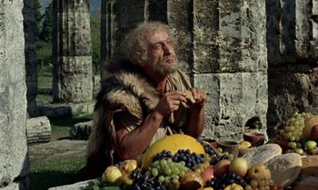 Movie still from “Jason and the Argonauts” (1963), directed by Don Chaffey – An old man eating a piece of food near a pile of fruit; Medium shot, Low angle