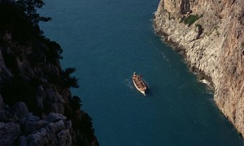 Movie still from “Jason and the Argonauts” (1963), directed by Don Chaffey – A boat floating on top of a body of water near some rocks; Extreme Wide shot, Overhead angle