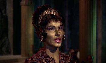 Movie still from “Jason and the Argonauts” (1963), directed by Don Chaffey – A woman with a gold face paint is wearing a red and gold outfit; Close Up shot, Over the shoulder angle