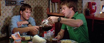 Movie still from “Jaws 3-D” (1983), directed by Joe Alves – Two men are sitting at a dinner table and one is pouring a jar of sauce; Medium shot, Low angle