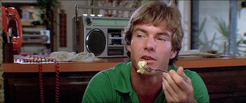 Movie still from “Jaws 3-D” (1983), directed by Joe Alves – A man eating a piece of food while sitting in front of a radio; Close Up shot, Low angle