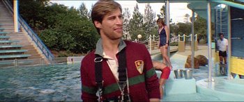 Movie still from “Jaws 3-D” (1983), directed by Joe Alves – A young man in a red and green sweater is standing in a pool of water; Medium shot, Low angle