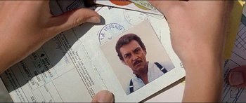 Movie still from “Jaws 3-D” (1983), directed by Joe Alves – A person holding a passport with a picture of a man in it; Extreme Close Up shot, Overhead angle