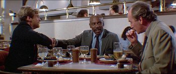 Movie still from “Jaws 3-D” (1983), directed by Joe Alves – A man sitting at a table with a plate in front of him; Medium shot, Low angle