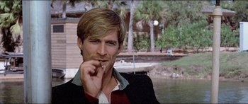 Movie still from “Jaws 3-D” (1983), directed by Joe Alves – A person smoking a cigarette near a body of water; Close Up shot, Over the shoulder angle
