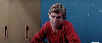 Movie still from “Jaws 3-D” (1983), directed by Joe Alves – A man in a red shirt is sitting in front of a blue wall; Close Up shot, Low angle