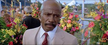Movie still from “Jaws 3-D” (1983), directed by Joe Alves – A man in a suit and tie standing in front of flowers; Close Up shot, Low angle