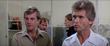 Movie still from “Jaws 3-D” (1983), directed by Joe Alves – A group of men standing next to each other in front of a fence; Close Up shot, Over the shoulder angle