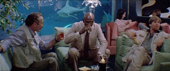 Movie still from “Jaws 3-D” (1983), directed by Joe Alves – A man sitting in a chair in front of a fish tank; Medium shot, Low angle