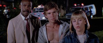 Movie still from “Jaws 3-D” (1983), directed by Joe Alves – A man with no shirt is standing in front of a group of people on the street; Close Up shot, Low angle
