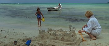 Movie still from “Jaws: The Revenge” (1987), directed by Joseph Sargent – A girl in a bathing suit standing in front of a sandcastle; Wide shot, High angle