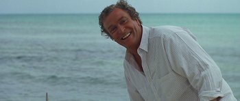 Movie still from “Jaws: The Revenge” (1987), directed by Joseph Sargent – A man with curly hair smiling at the beach; Close Up shot, Over the shoulder angle
