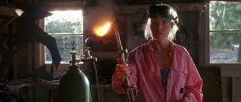 Movie still from “Jaws: The Revenge” (1987), directed by Joseph Sargent – A woman in a pink shirt holding a blow torch in her hand; Medium shot, Low angle