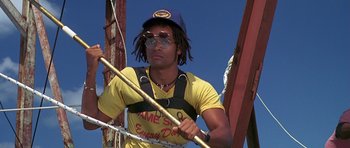 Movie still from “Jaws: The Revenge” (1987), directed by Joseph Sargent – A man in yellow shirt and blue hat holding a pole; Medium shot, Low angle
